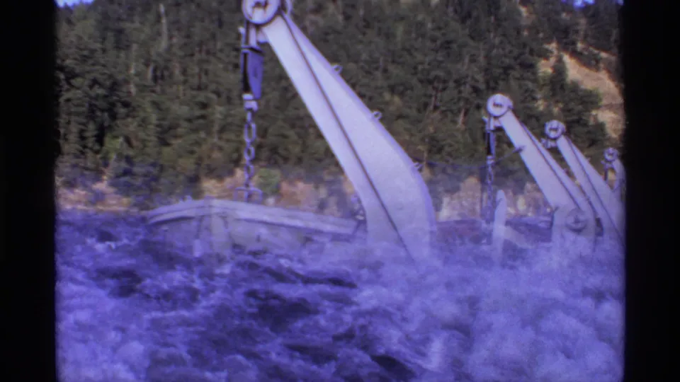 1974 Canadian ferry footage showing lifeboats and davit arms above foaming water, with wooded hills in the background.
