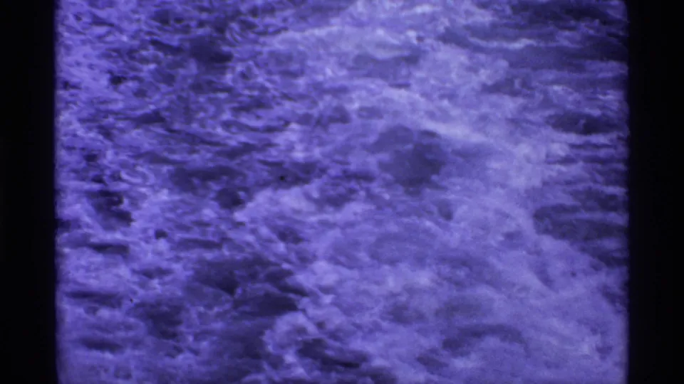 Purple-shifted 8mm frame of rough foaming wake trailing behind a vessel in the 1974 Canada ferry clip.