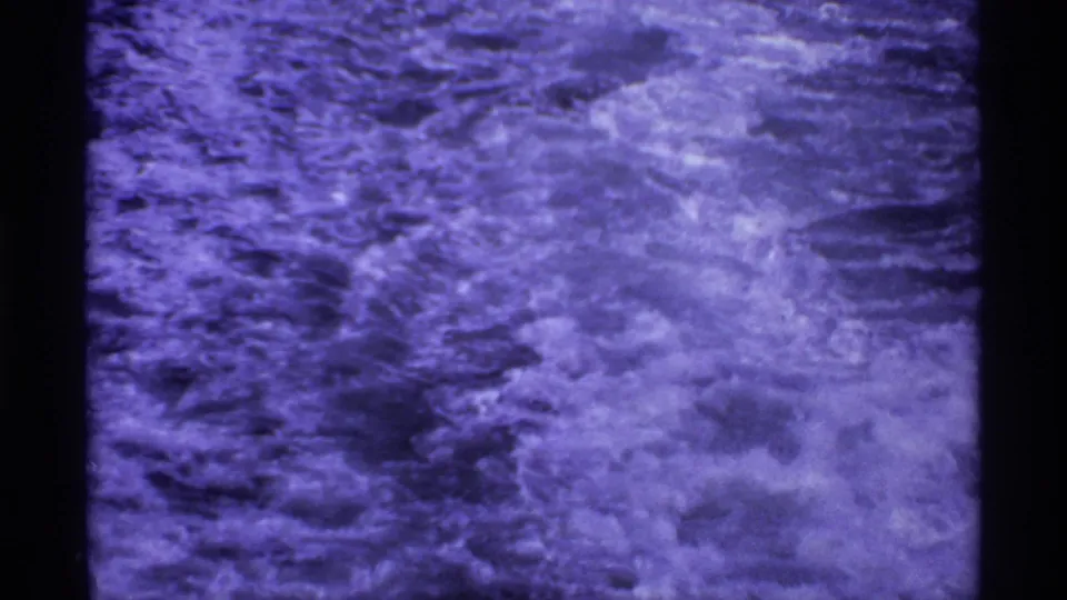 Purple-blue 8mm view of turbulent ferry wake, with the frame dominated by churning water and film texture.