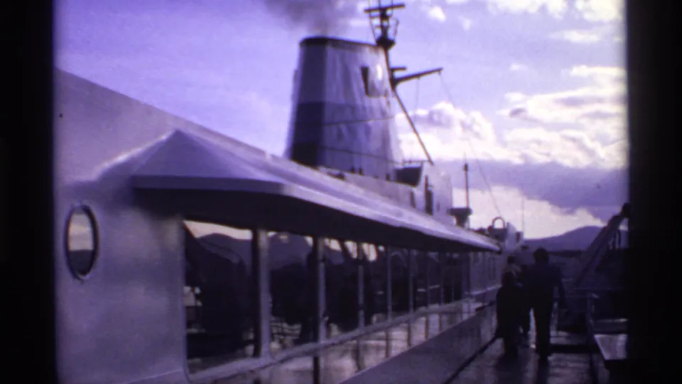 1974 Canadian 8mm frame of a ship side and promenade deck, with a round porthole and passengers beneath the smoking funnel.