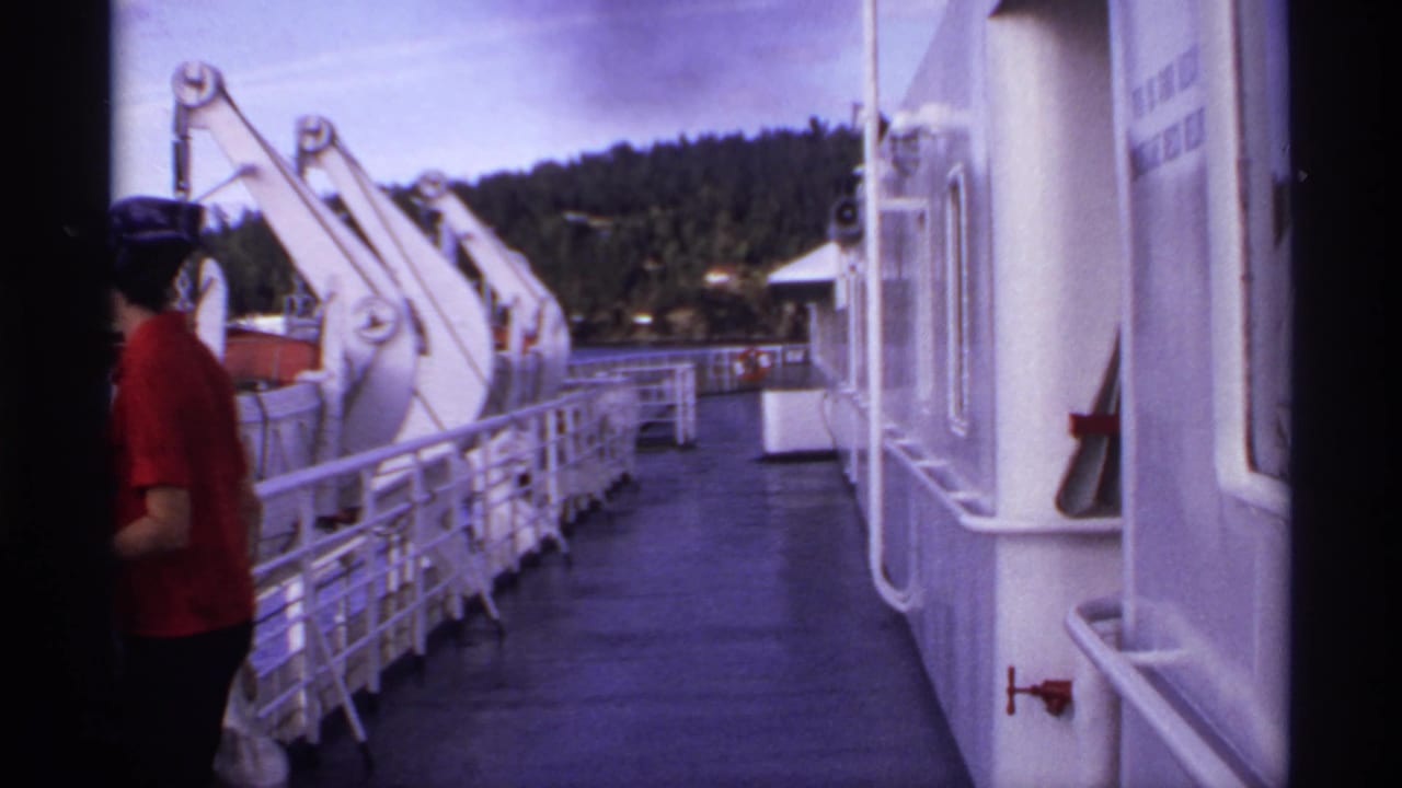 Woman seen from behind walking away on a ferry deck beside white ship structures.