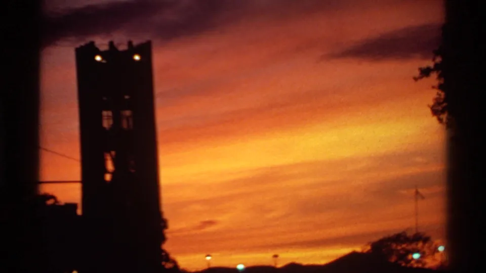 1974 Canadian 8mm frame of a tower and trees in silhouette against a vivid orange sunset and low hills.