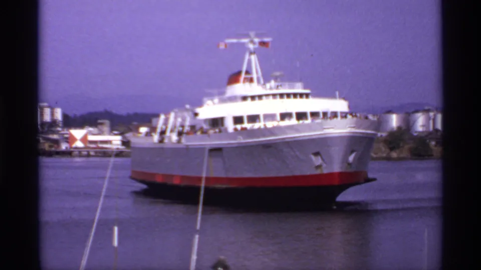 Large red-and-white ferry at a Canadian seaport in 1974, captured with soft 8mm color and industrial waterfront details behind it.