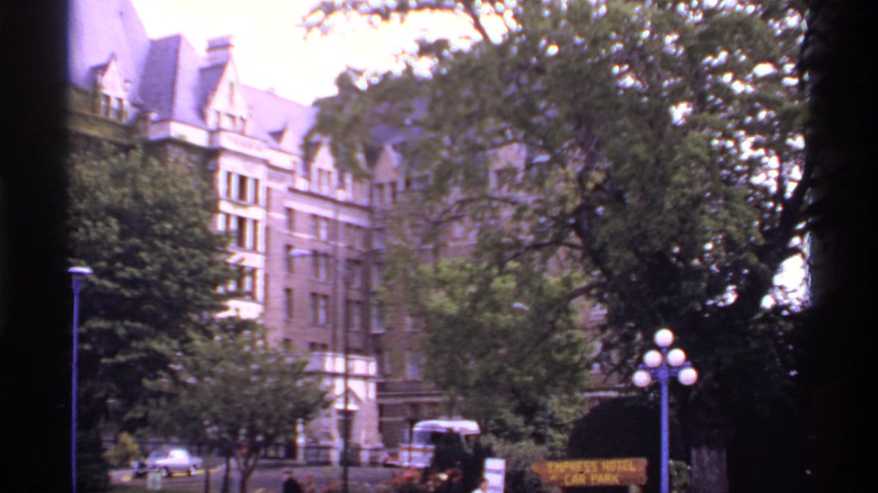 Ornate hotel facade beside trees, street lamps, cars, and a small parking sign at the curb.