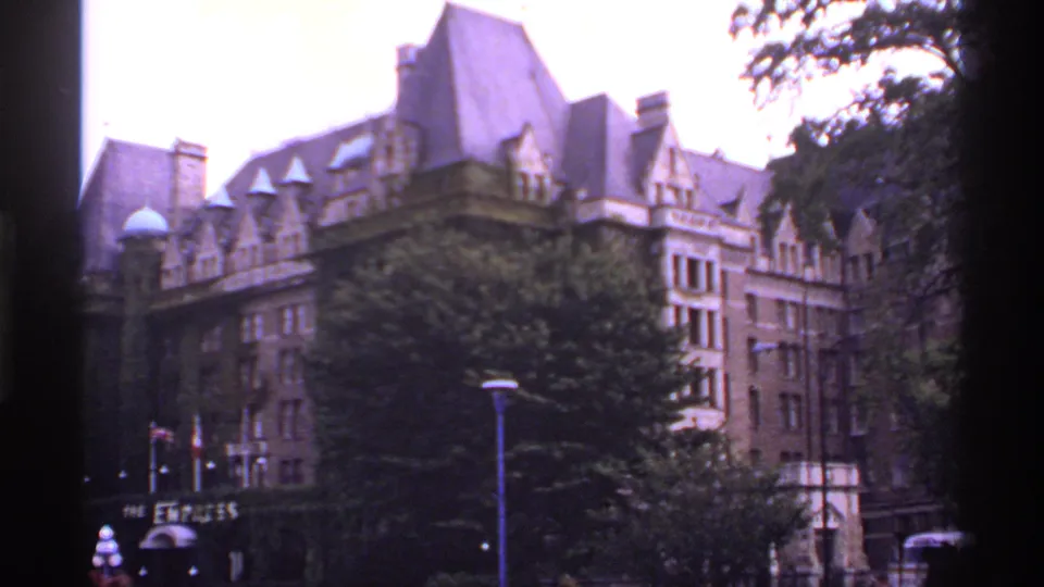 1974 Canada 8mm frame showing a wider view of The Empress hotel, its ivy-covered lower facade, entrance sign, trees, and street activity.