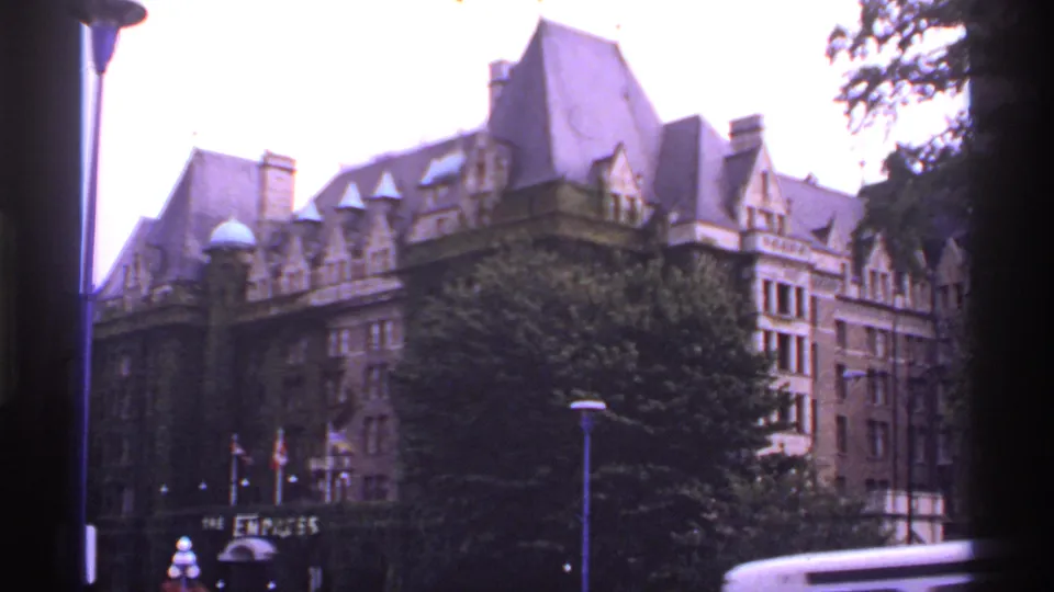 1974 8mm Canada frame with a historic-looking building, heavy tree cover, flags, lamps, and dark film borders visible.