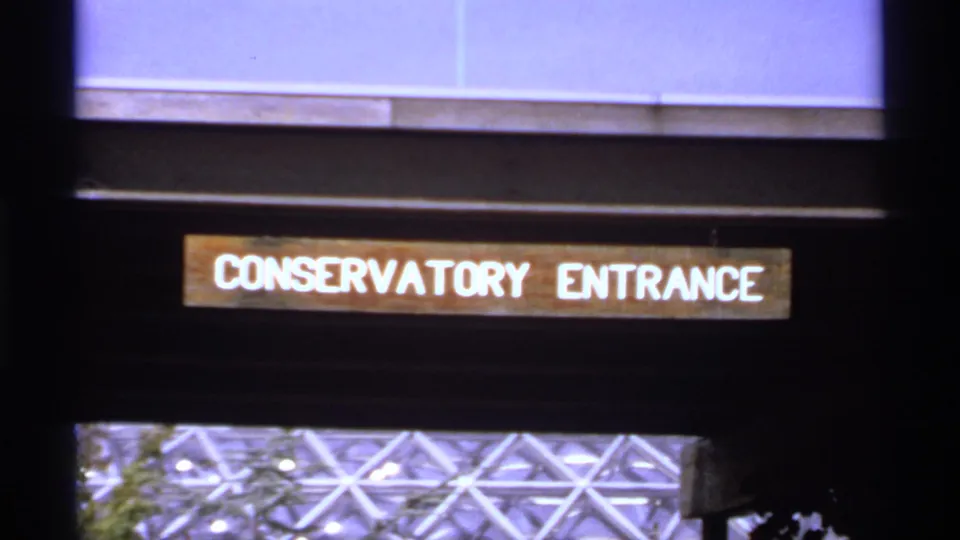 1974 Canada 8mm frame showing a readable Conservatory Entrance sign below a modern glass facade.