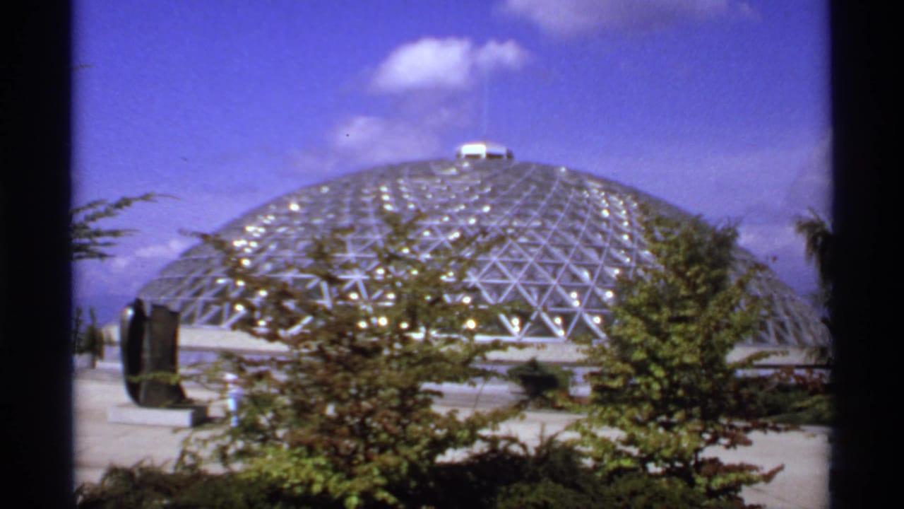 Geodesic glass dome under a blue sky with trees in the foreground.