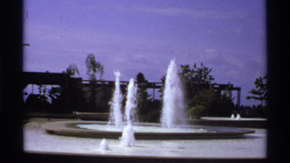 1974 Canadian home-movie frame showing multiple fountain jets against trees and a dark background structure.