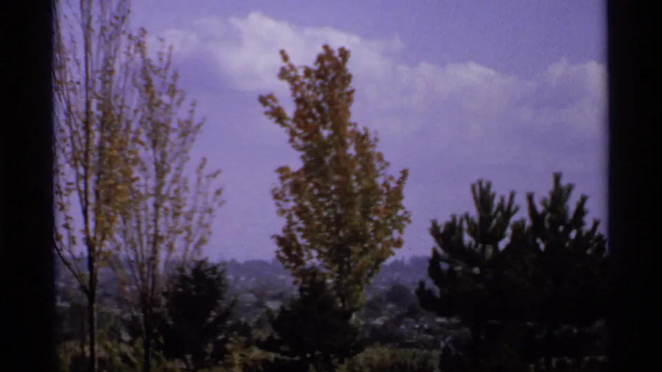 1974 Canadian 8mm frame looking past porch framing toward trees and a hazy purple-blue sky.