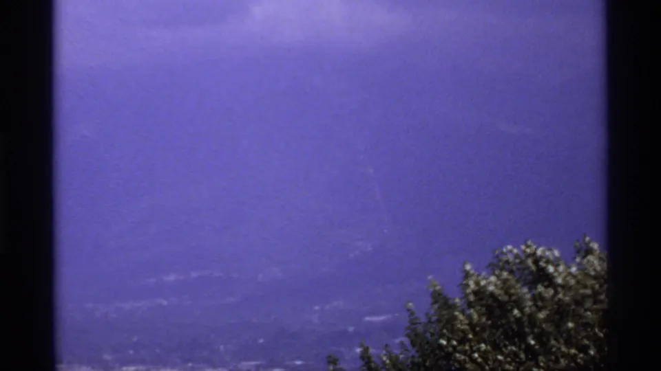 1974 Canada 8mm frame showing a saturated purple-blue summit panorama with treetops and visible home-movie frame edges.