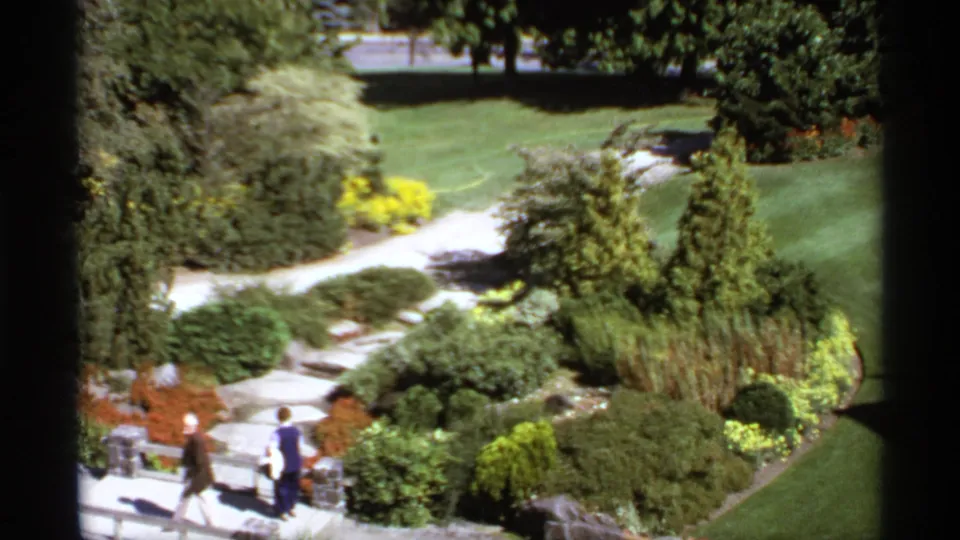1974 Canada 8mm frame showing a landscaped park with paths, lawns, shrubs, and distant visitors viewed from above.