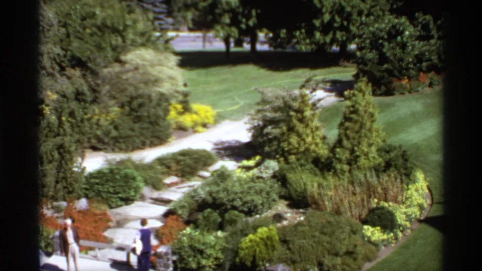 Elevated 1974 Canada park view with manicured plantings, winding paths, and visitors partly visible at the lower frame edge.