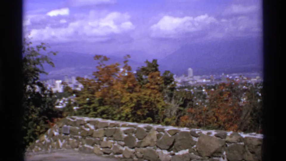 1974 Canada 8mm frame showing a distant city skyline from a hilltop lookout, framed by autumn trees and a stone wall.