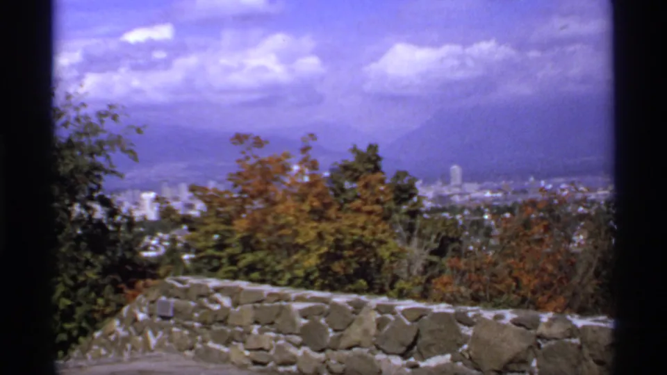 1974 Canadian 8mm view of a city and distant mountains framed by autumn trees and a low stone wall.