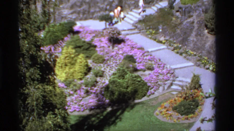 1974 Canada 8mm view over a formal garden with paths, purple flowers, shrubs, lawn, stairs, and small distant visitors.