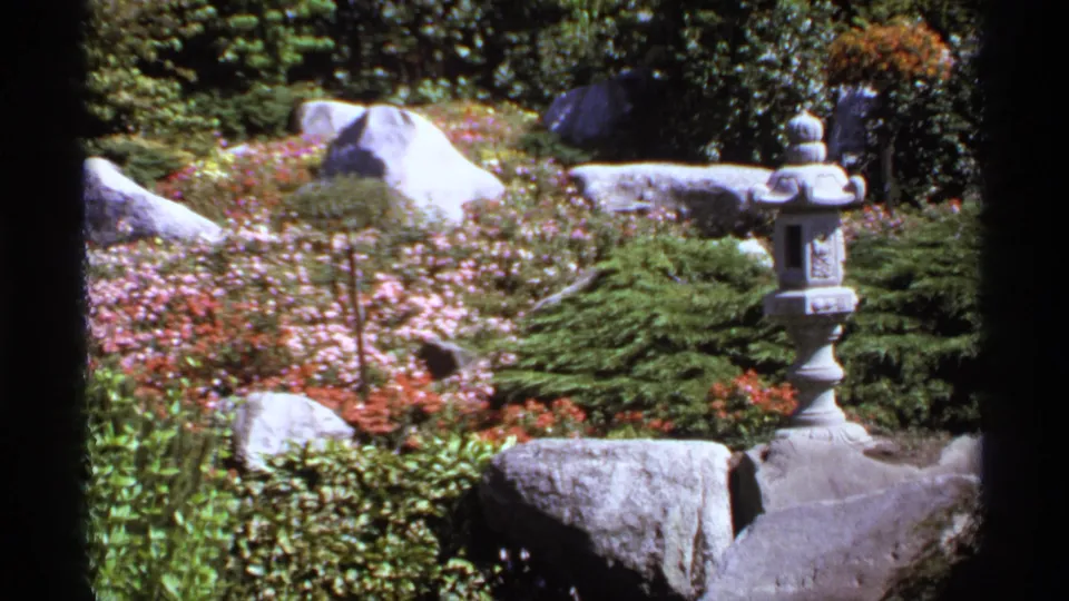 1974 Canada garden frame showing a stone lantern partly near the edge, with boulders, low greenery, and flower beds.