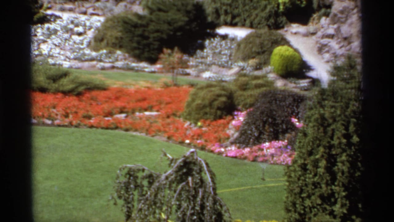 Formal garden with red flower beds, green lawn, shrubs, paths, and dark frame edges.