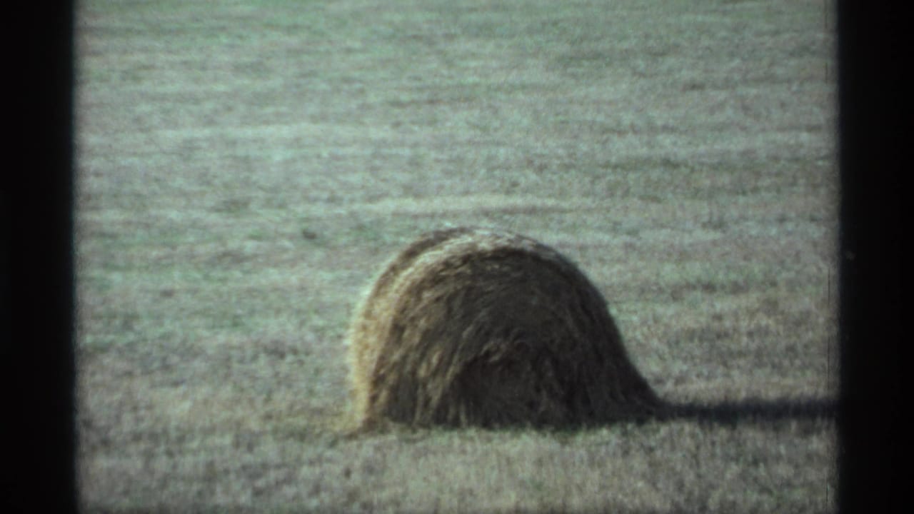 A large hay bale rests in a harvested Minnesota field in 1974, seen through soft, grainy 8mm home-movie footage.