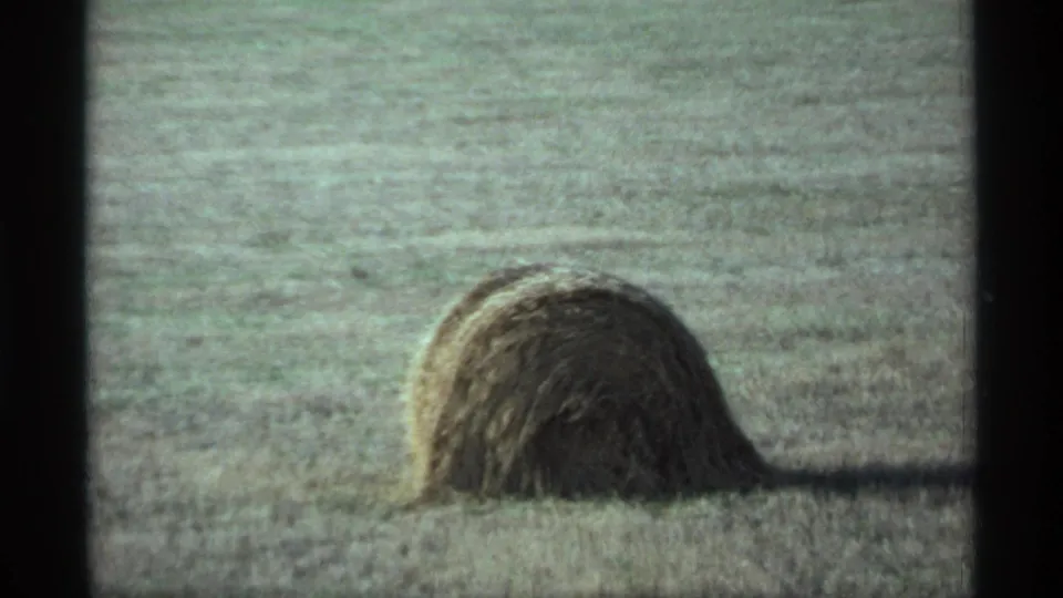 A large hay bale rests in a harvested Minnesota field in 1974, seen through soft, grainy 8mm home-movie footage.