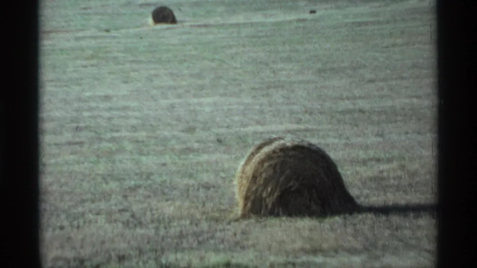 A foreground hay bale sits in a harvested Minnesota field, with another bale visible in the distance on 8mm film.