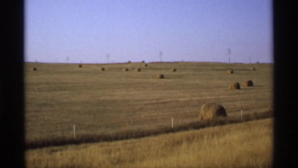 1974 Minnesota 8mm frame showing a harvested hay field with round bales, fence posts, and a clear sky.