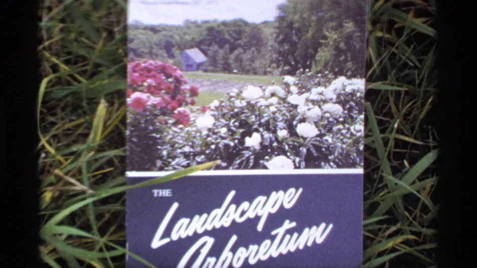 A 1970s home-movie close-up of The Landscape Arboretum brochure, with garden flowers and surrounding grass visible.
