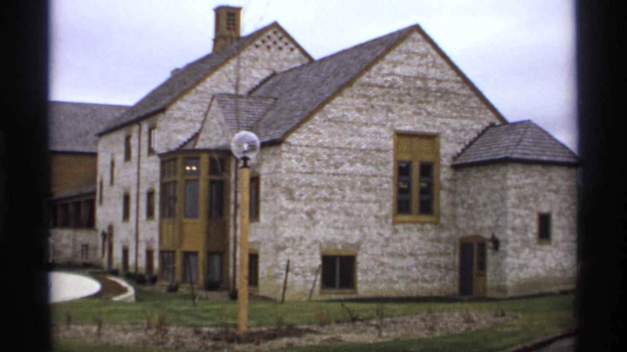 Stone building with yellow-brown window trim, globe lamppost, lawn, and curved walkway.