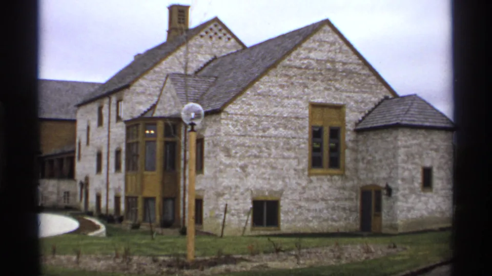 1974 Minnesota 8mm frame showing a large stone building with tan trim, bay window, globe lamppost, lawn, and curved path.