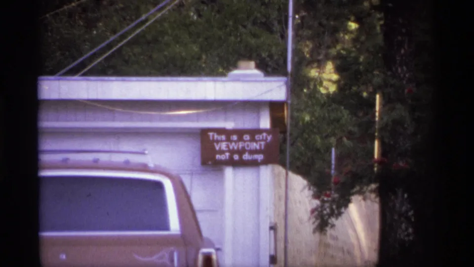 1974 Spokane exterior frame with a brown car partly blocking a white garage and a sign reading "This is a city VIEWPOINT not a dump."