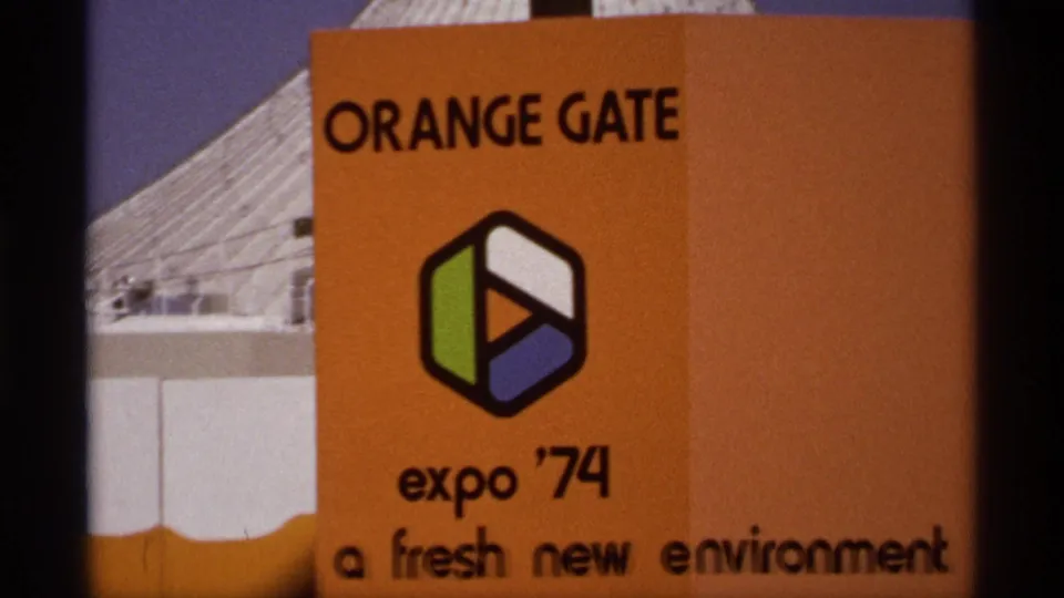 Spokane Expo '74 Orange Gate entrance sign with event logo, orange panel, and partial fair building in 1974 8mm footage.
