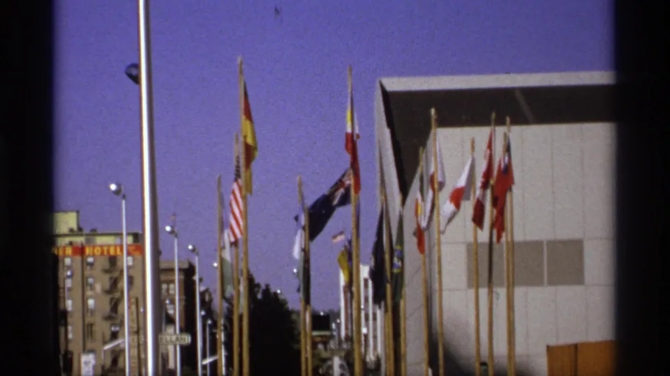 Expo '74 flag display beside a modern fair building in Spokane, captured in saturated 1970s 8mm color.