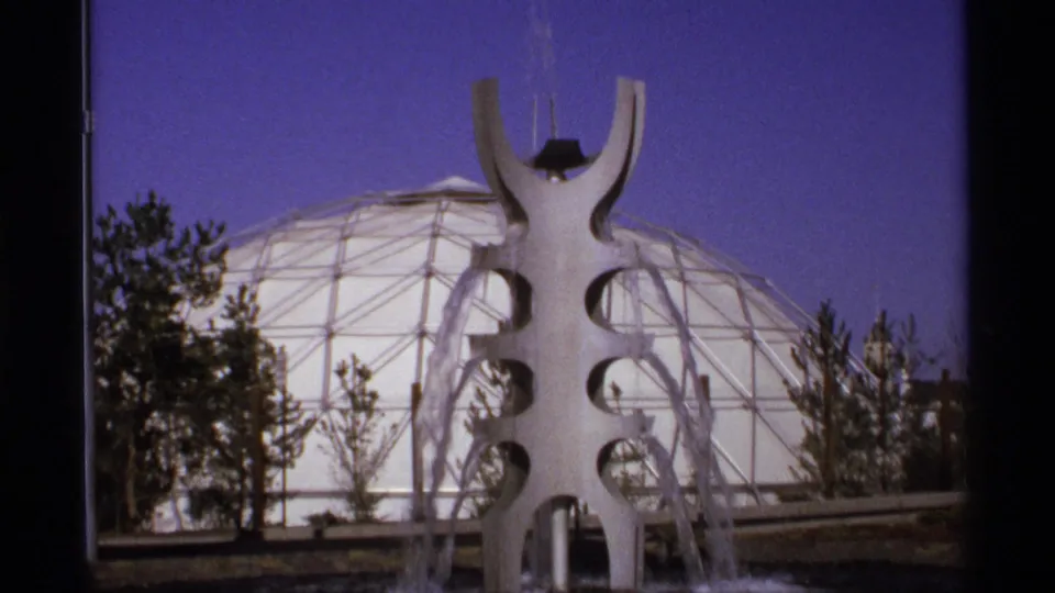 Modern sculptural fountain stands before a geodesic dome and trees at the Spokane Expo '74 fairgrounds.