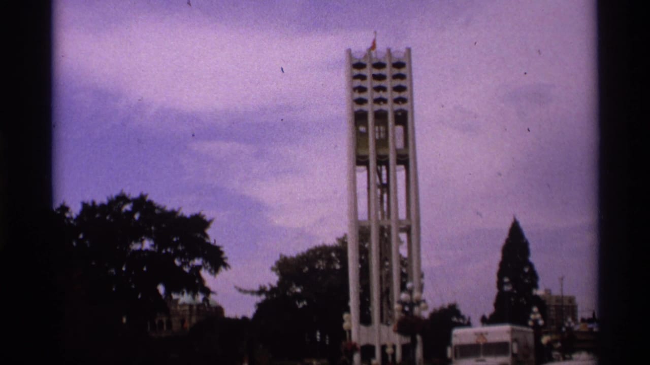 1974 Vancouver 8mm frame showing a tall modernist bell tower above tree silhouettes with a white van near the base.