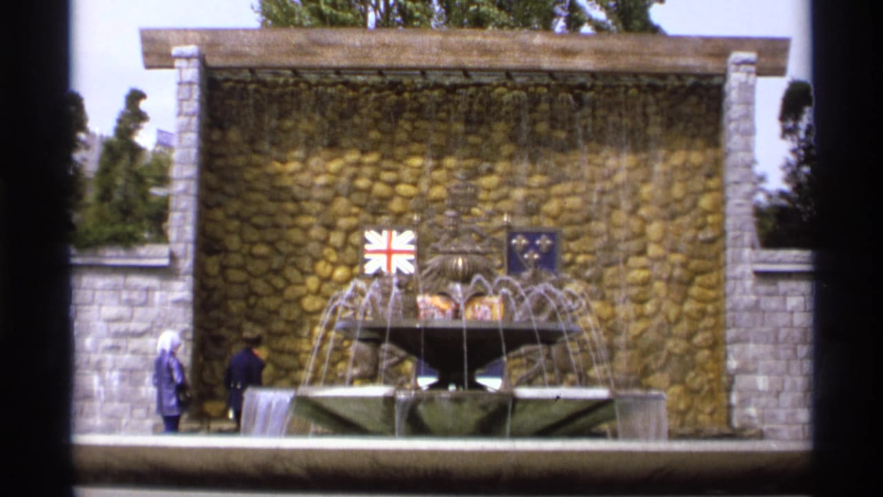 Stone fountain before a textured wall with small flags and two distant pedestrians.