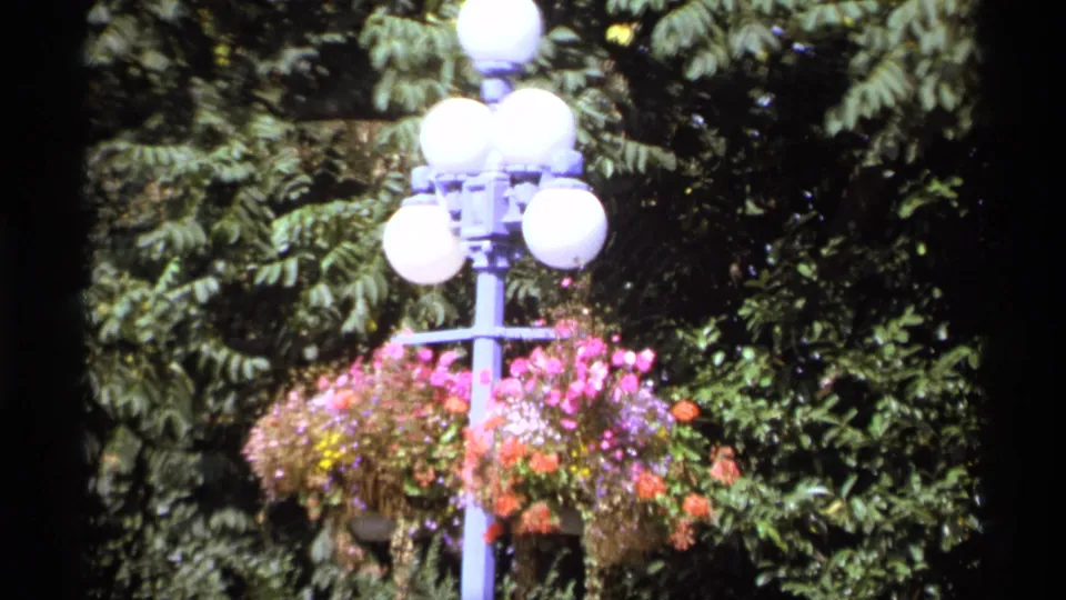 Soft 8mm frame of a blue lamppost, white globe lights, and colorful hanging baskets in Vancouver, 1974.