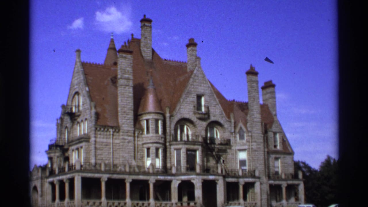 Grand stone building with red-brown roof, chimneys, arched windows, and blue sky.