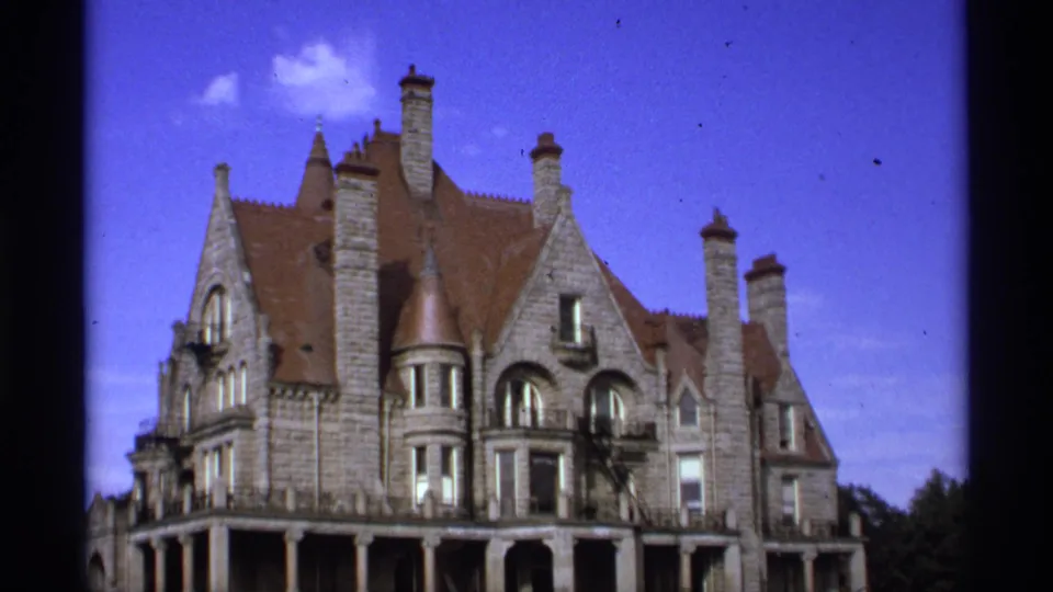 1974 Vancouver frame with the building facade held in a wide view, showing steep roof sections, chimneys, arched windows, and a small tower.