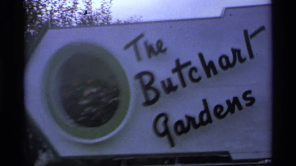 Close view of The Butchart Gardens sign in 1974 8mm footage, with a circular emblem and hand-lettered black text.