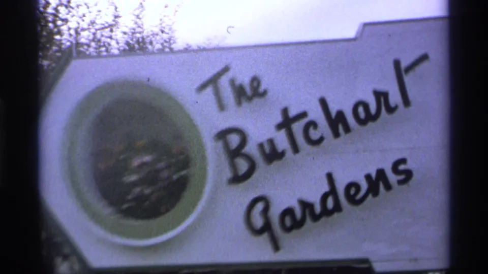 1974 home-movie frame showing The Butchart Gardens sign close-up, with visible logo-style lettering and a circular graphic at left.