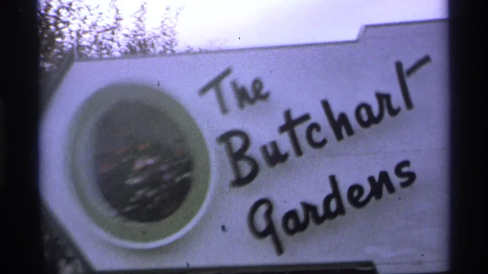 1974 8mm frame showing a white The Butchart Gardens sign with black cursive lettering and a circular floral inset.