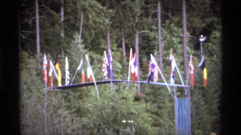 1974 Vancouver 8mm view of a multi-flag outdoor display framed by trees and garden vegetation.