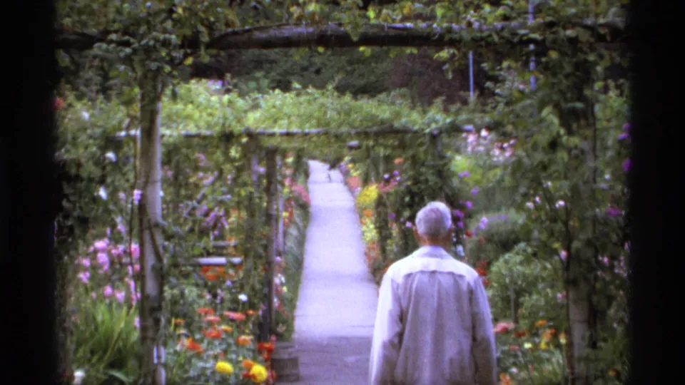 An adult visitor seen from behind on a Vancouver garden path, with flowers and greenery lining the walkway.