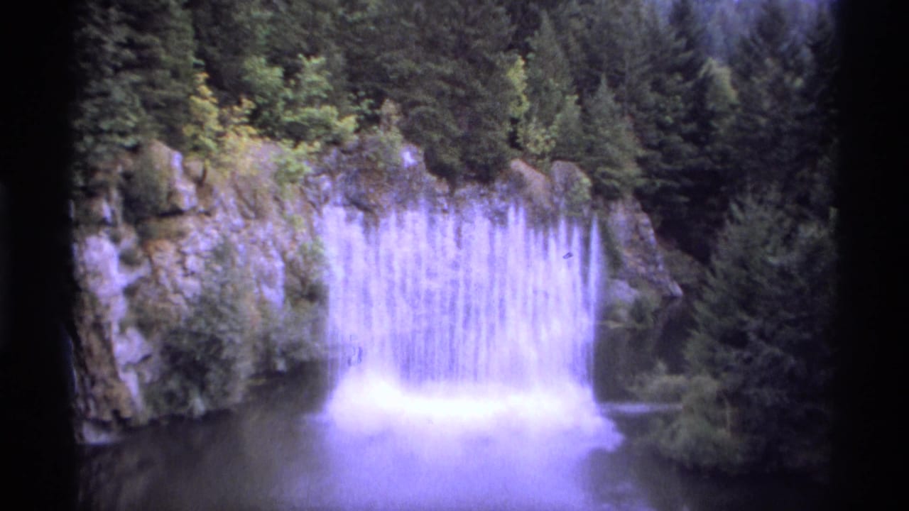 Waterfall dropping from a rocky ledge into a dark pool surrounded by trees.