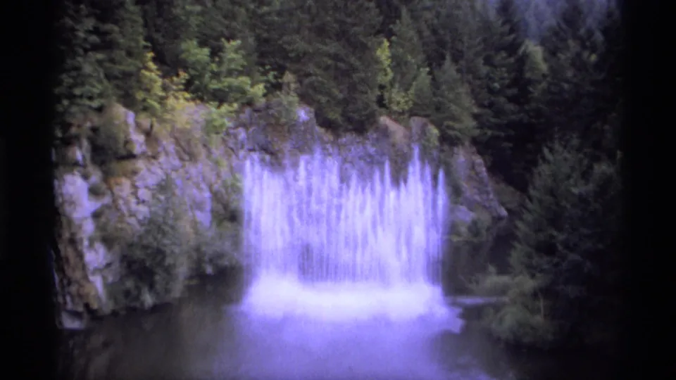 Vintage 8mm view of a waterfall and pool near Vancouver, framed by rock walls and dark evergreen growth.