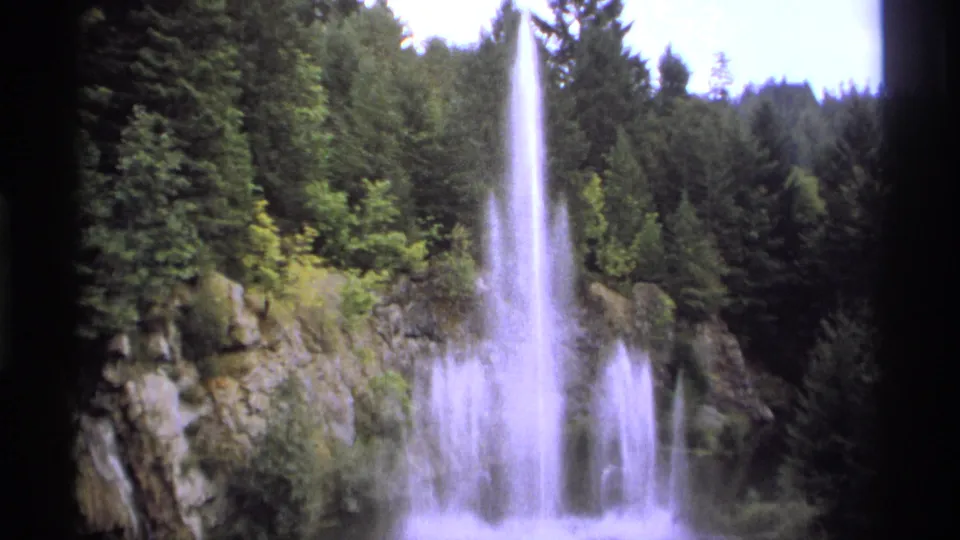1974 Vancouver-area 8mm frame with a wider fountain burst, tall spray, rock wall, and surrounding conifer forest.