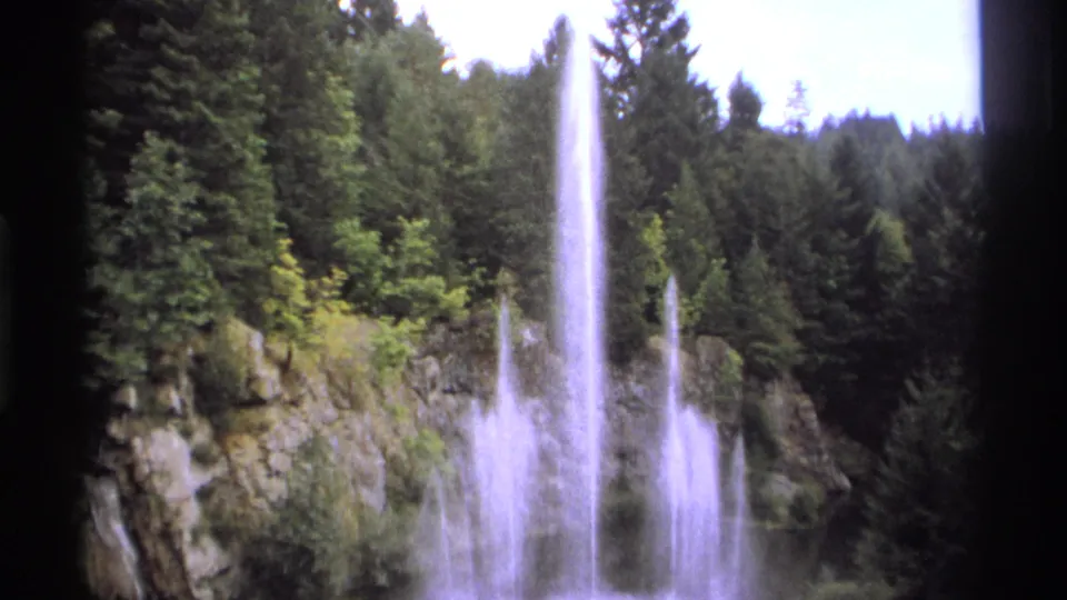 A steady 8mm view of the fountain in Vancouver, with several water jets backed by evergreens and stone.