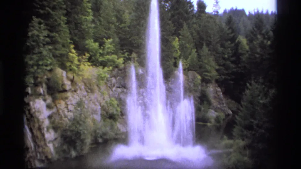 A vintage Vancouver park view shows the fountain's central jet and side sprays framed by trees, rocks, and film gate edges.
