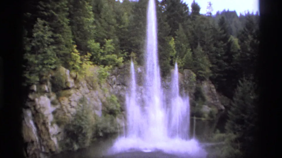 1974 Vancouver 8mm frame of a dramatic water spray beside rocks and evergreen trees, with soft focus and film borders.