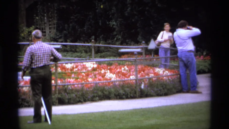 A 1974 Vancouver park view shows a man with a white cane near a flower bed while two adults stand across the path.